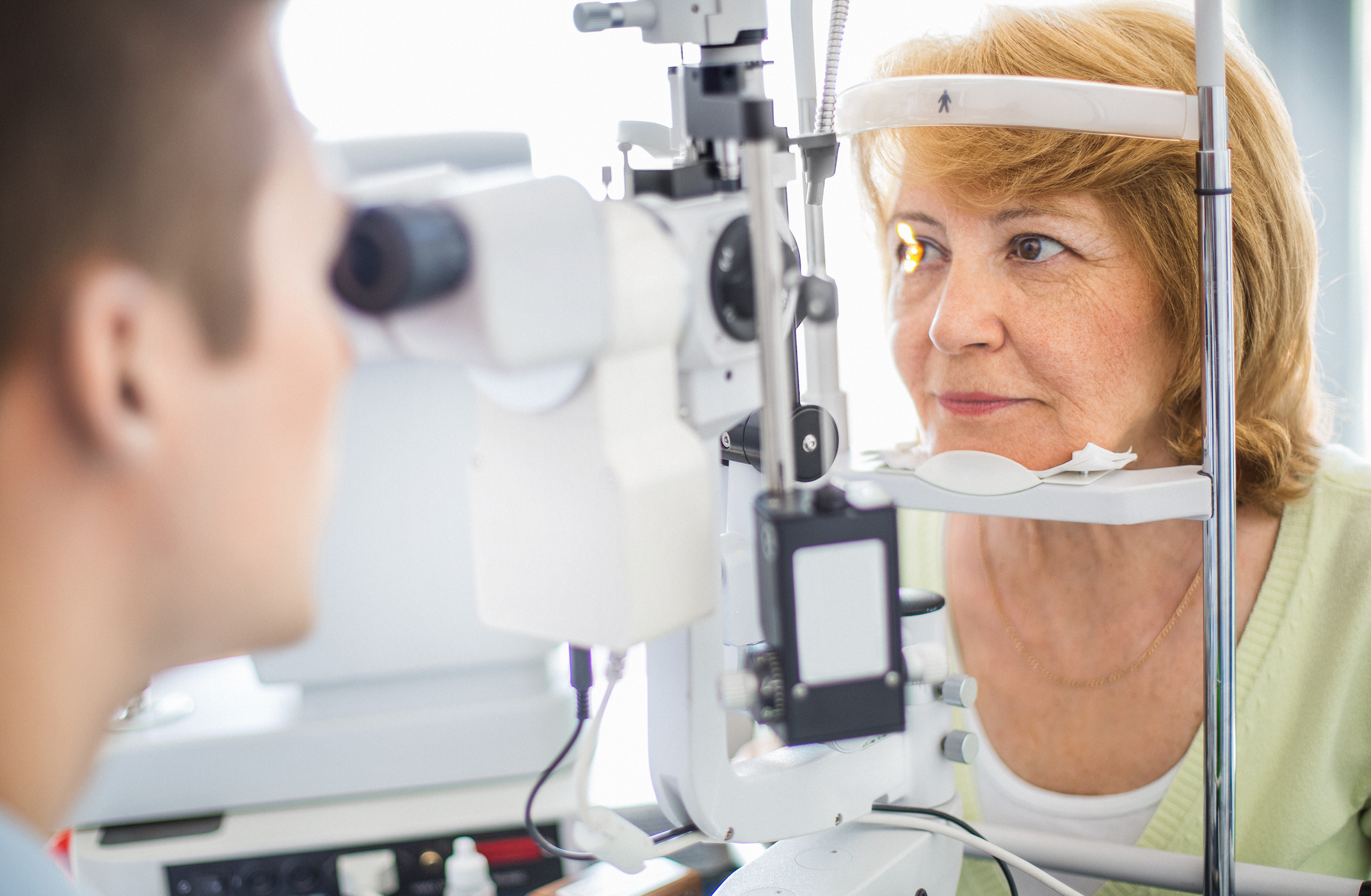 Optometrist assessing female right eye with equipment.